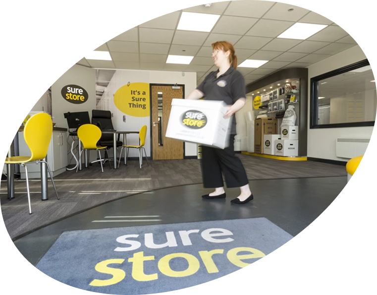 download-app-banner A staff member carrying a box in a modern office with yellow chairs and a carpet displaying the brand name 'sure store.' The office has a welcoming atmosphere with a clear view of branded signage.