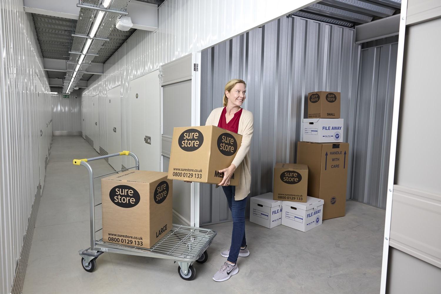 image_738220135_1 A woman pulling a cart with boxes labeled 'sure store' in a storage facility. The background features storage units with stacked boxes.